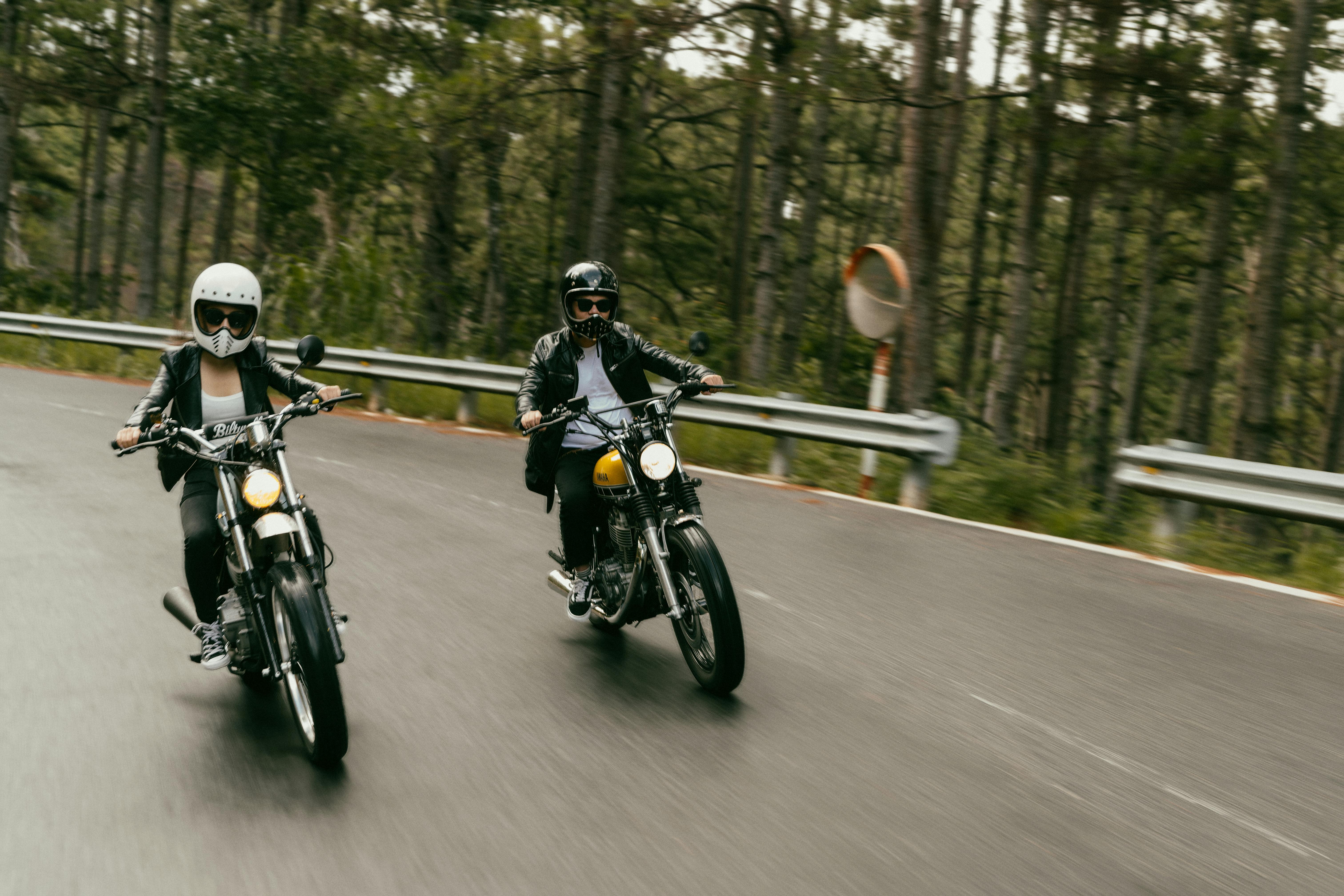 Two bikers riding motorbikes on a curvy forest road, capturing motion and excitement.