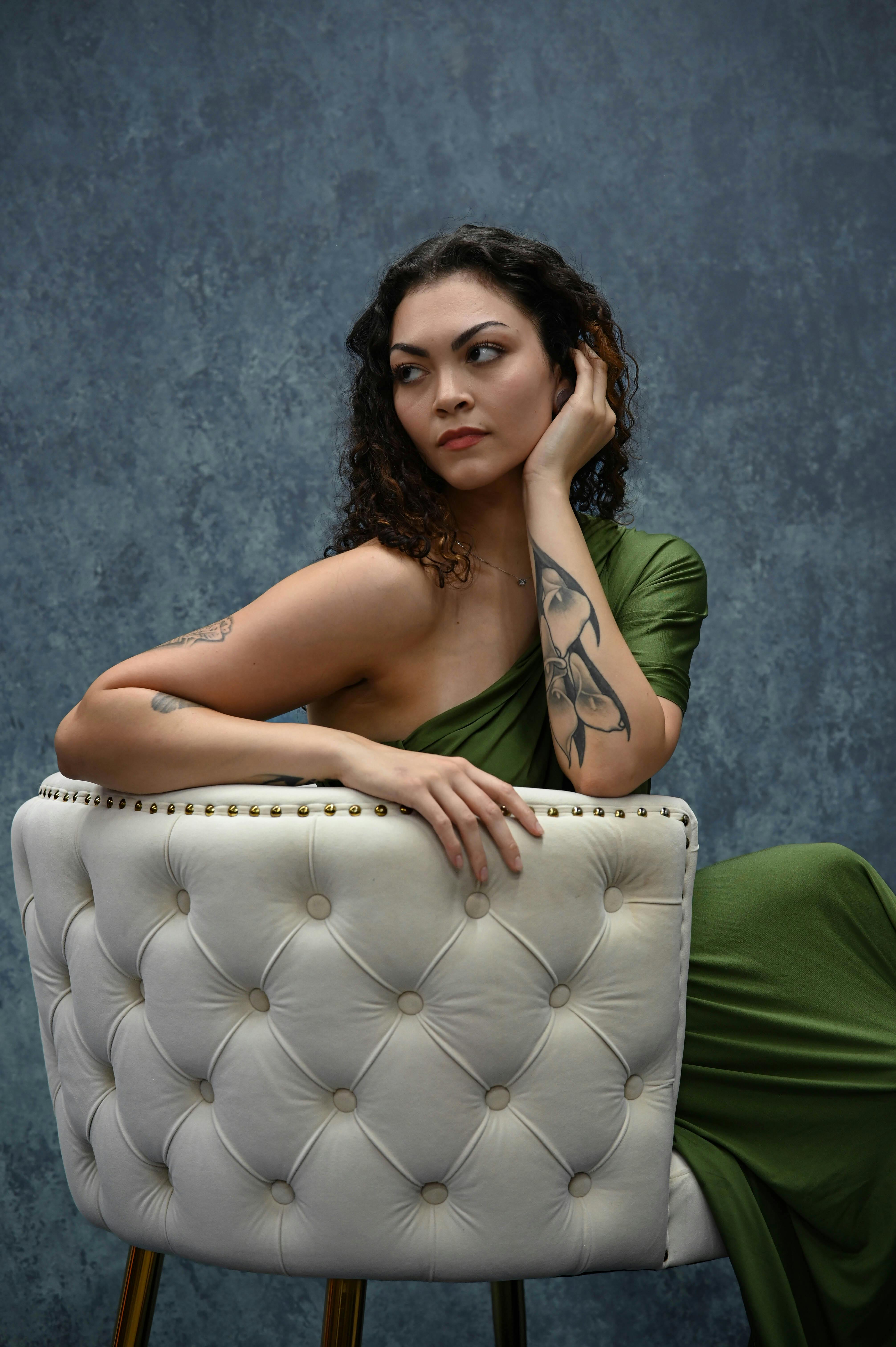 Elegant woman in green dress posing on a chic chair with a textured background, capturing modern charm.