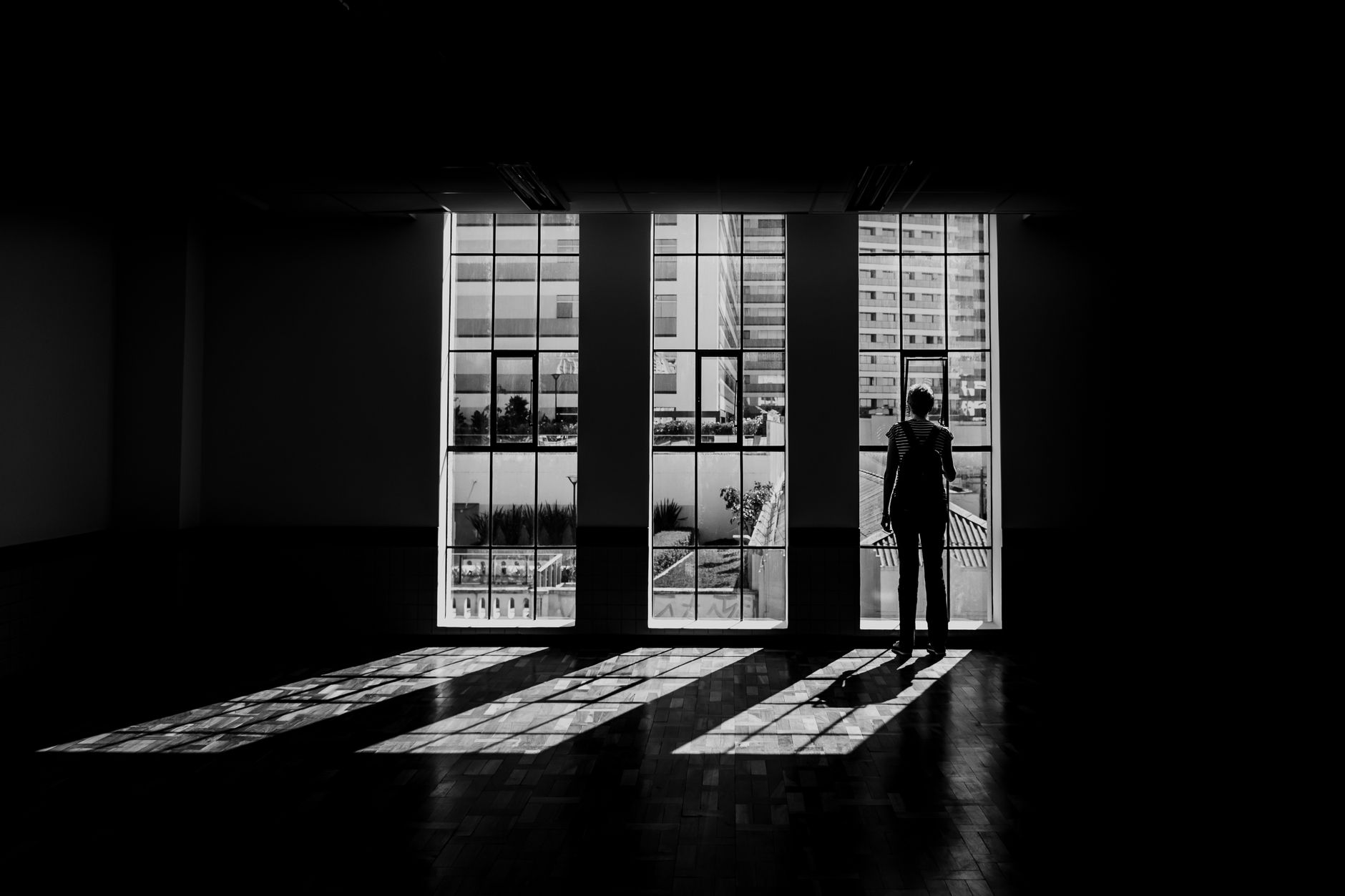 Dramatic black and white image of a silhouette in a modern room with large windows.