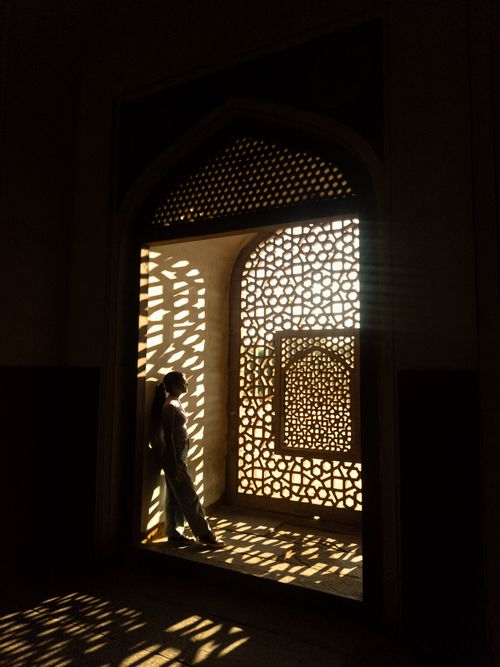 Free A person stands in a sunlit ornately patterned archway, casting shadows indoors. Stock Photo