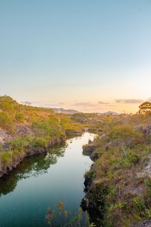 Free A peaceful sunset scene with a calm river reflecting the clear sky, surrounded by lush greenery. Stock Photo