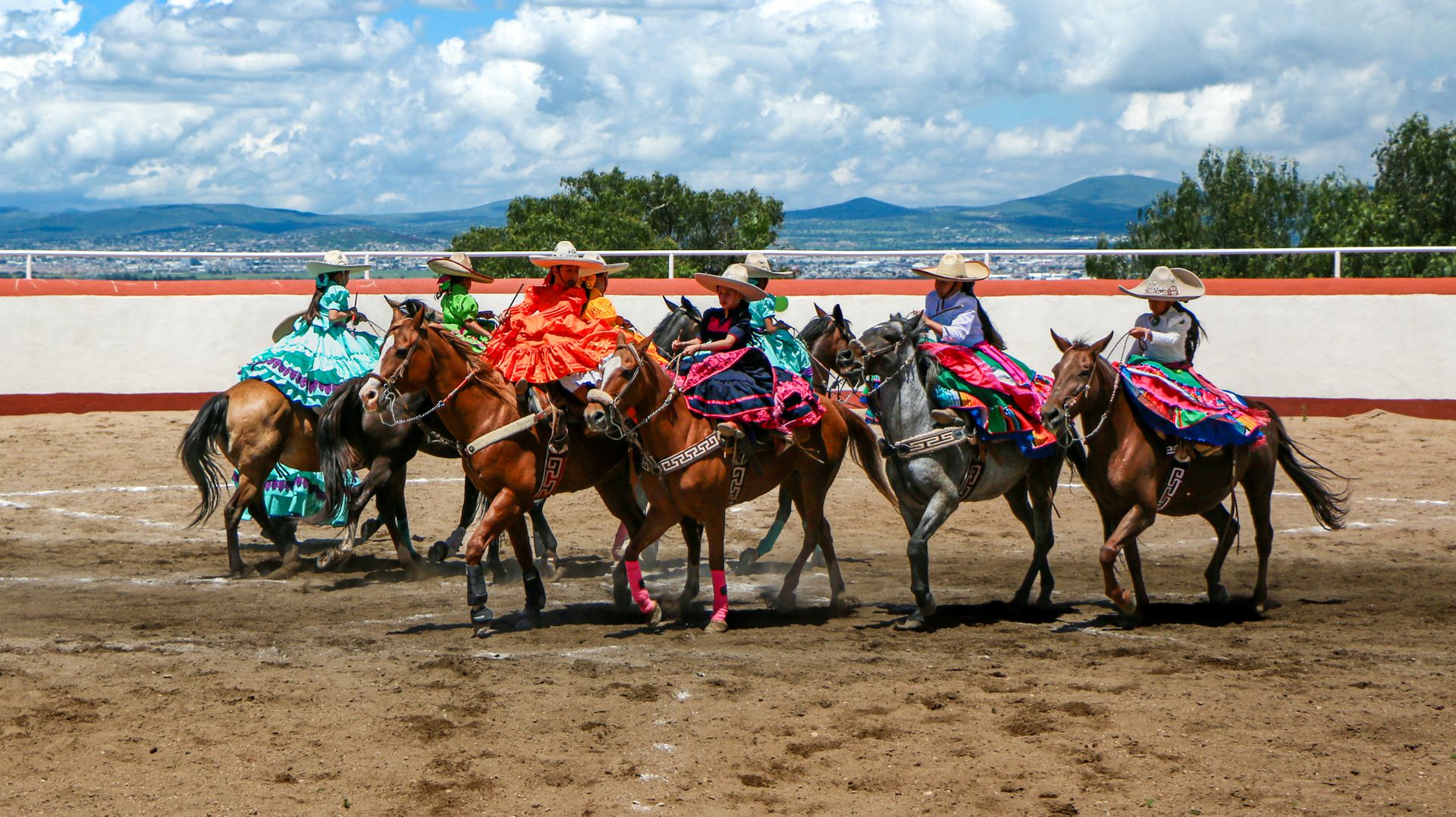 A group of people riding horses in a dirt arena