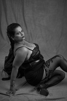 Black and white portrait of a woman in elegant lingerie and fishnet stockings, exuding confidence.