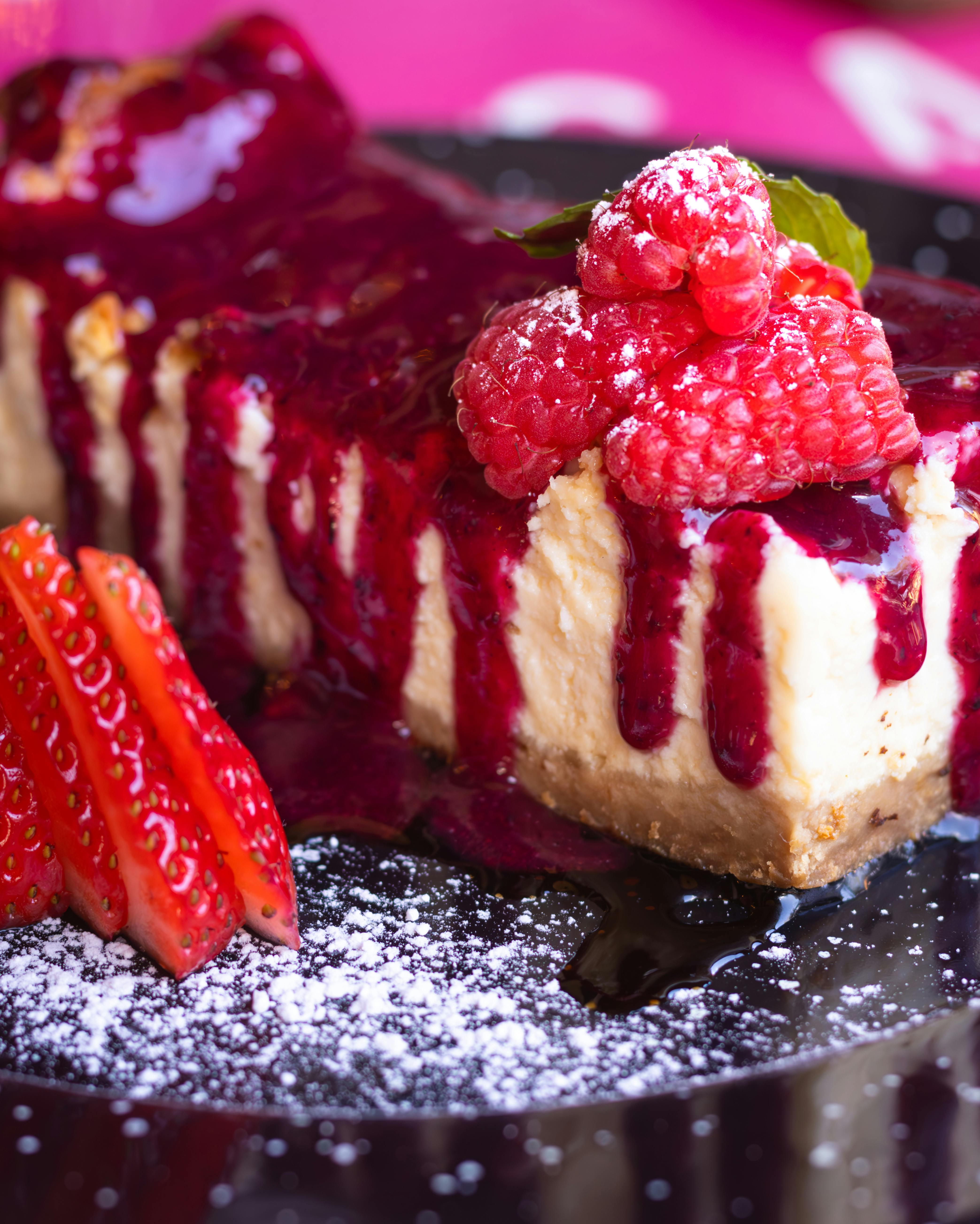 Tempting cheesecake topped with raspberries and strawberry slices, perfect dessert.