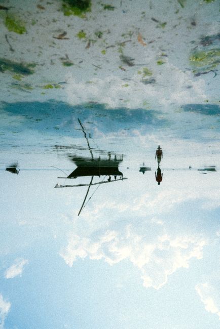 A serene reflection of a boat and figures on a calm beach during the day.