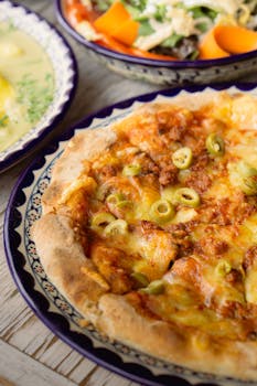 Tasty homemade pizza topped with cheese, sausage, and green olives served on a decorative plate.