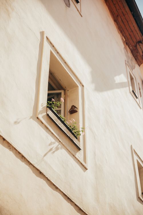 Free Sunlit facade of a rustic house with an open window and small plants. Stock Photo