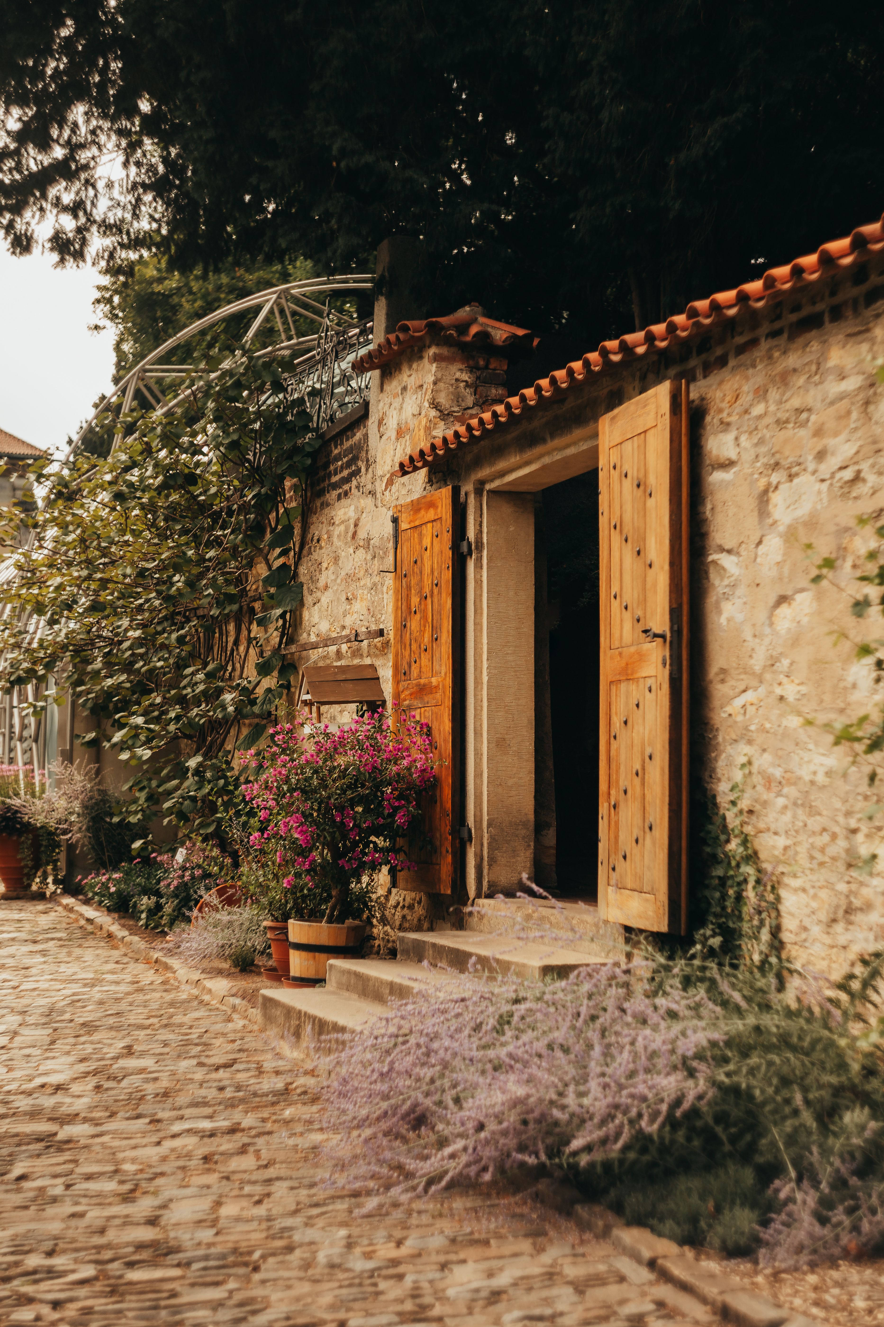 A beautiful rustic stone house with an open wooden door surrounded by lush greenery and flowers.