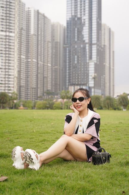 Young woman enjoying leisure time on a grassy field with city skyscrapers background.