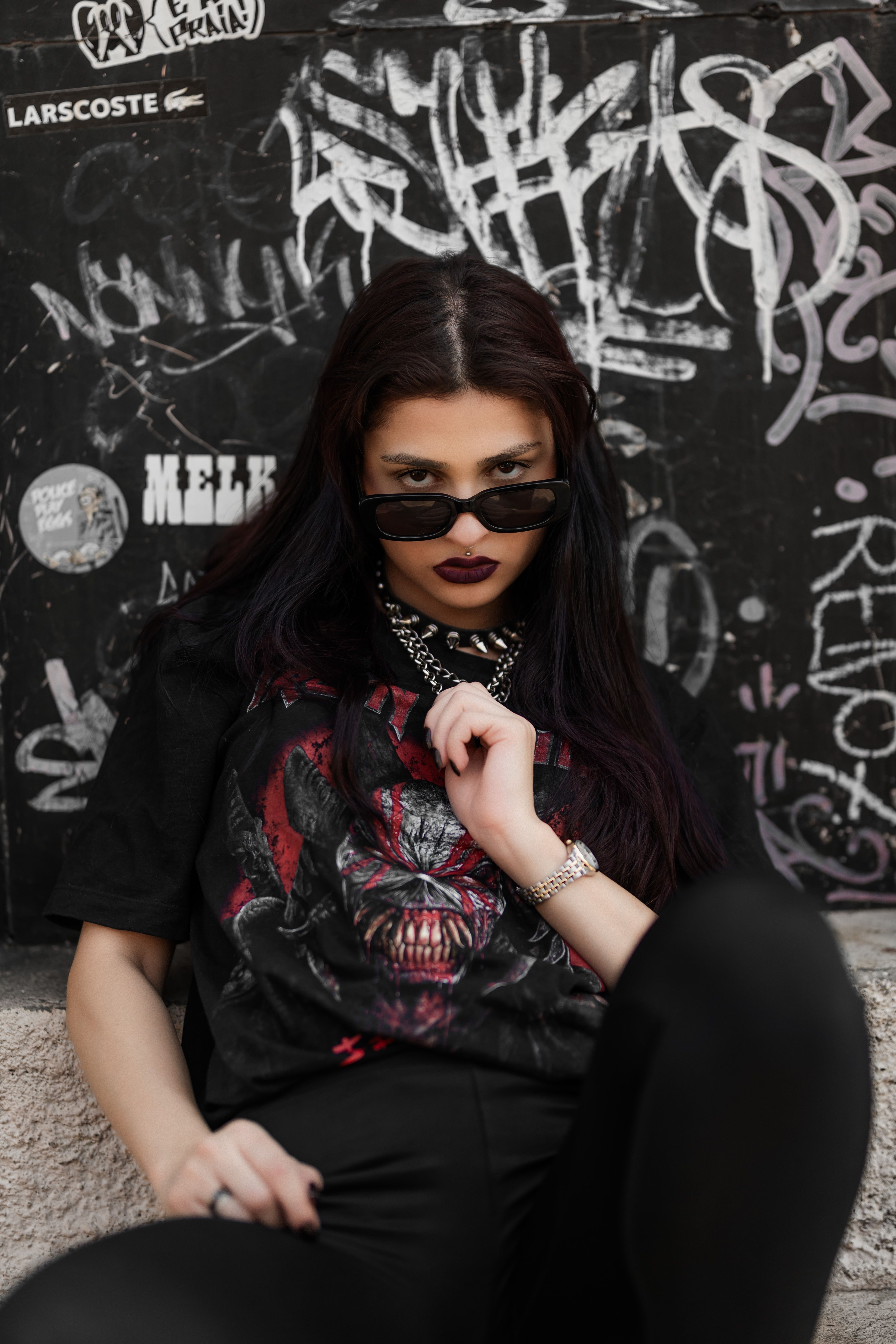 Fashionable woman in sunglasses poses against a graffiti wall in an urban setting.