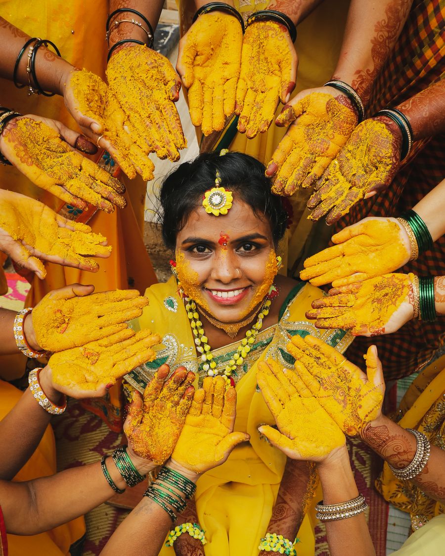 Bride smiling surrounded by turmeric-covered blessing hands