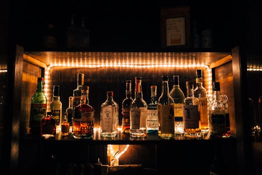 A stylish arrangement of various liquor bottles beautifully illuminated on a shelf in a dimly lit bar setting. by Kelly