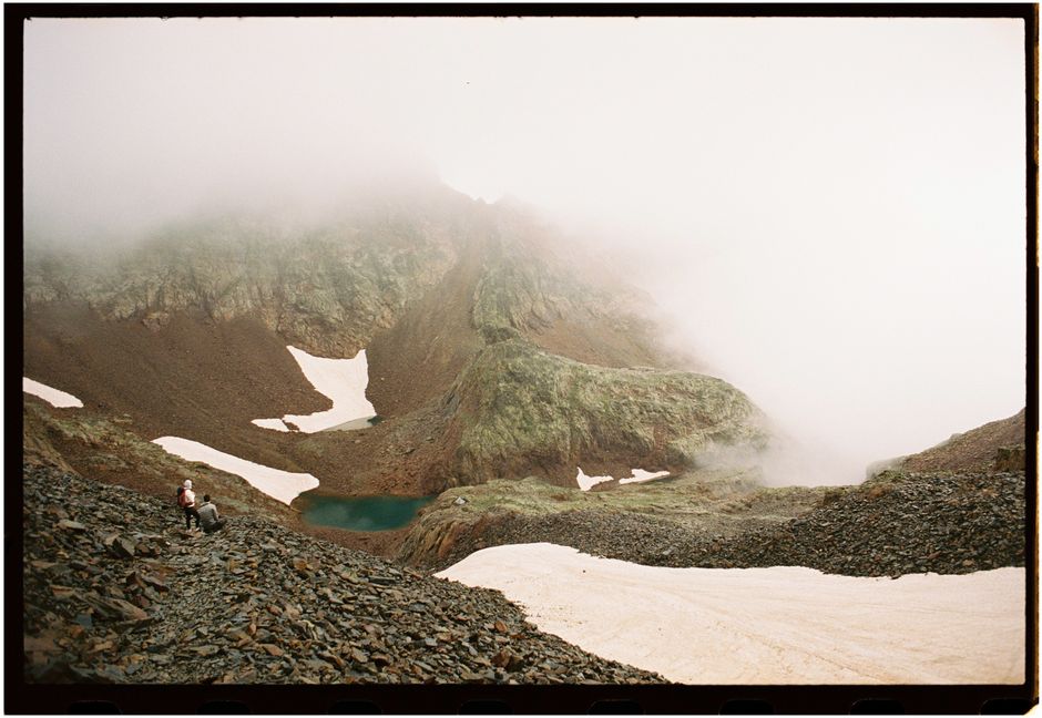 Hikers explore a misty mountain landscape in CT, Spain with peaks and lakes.