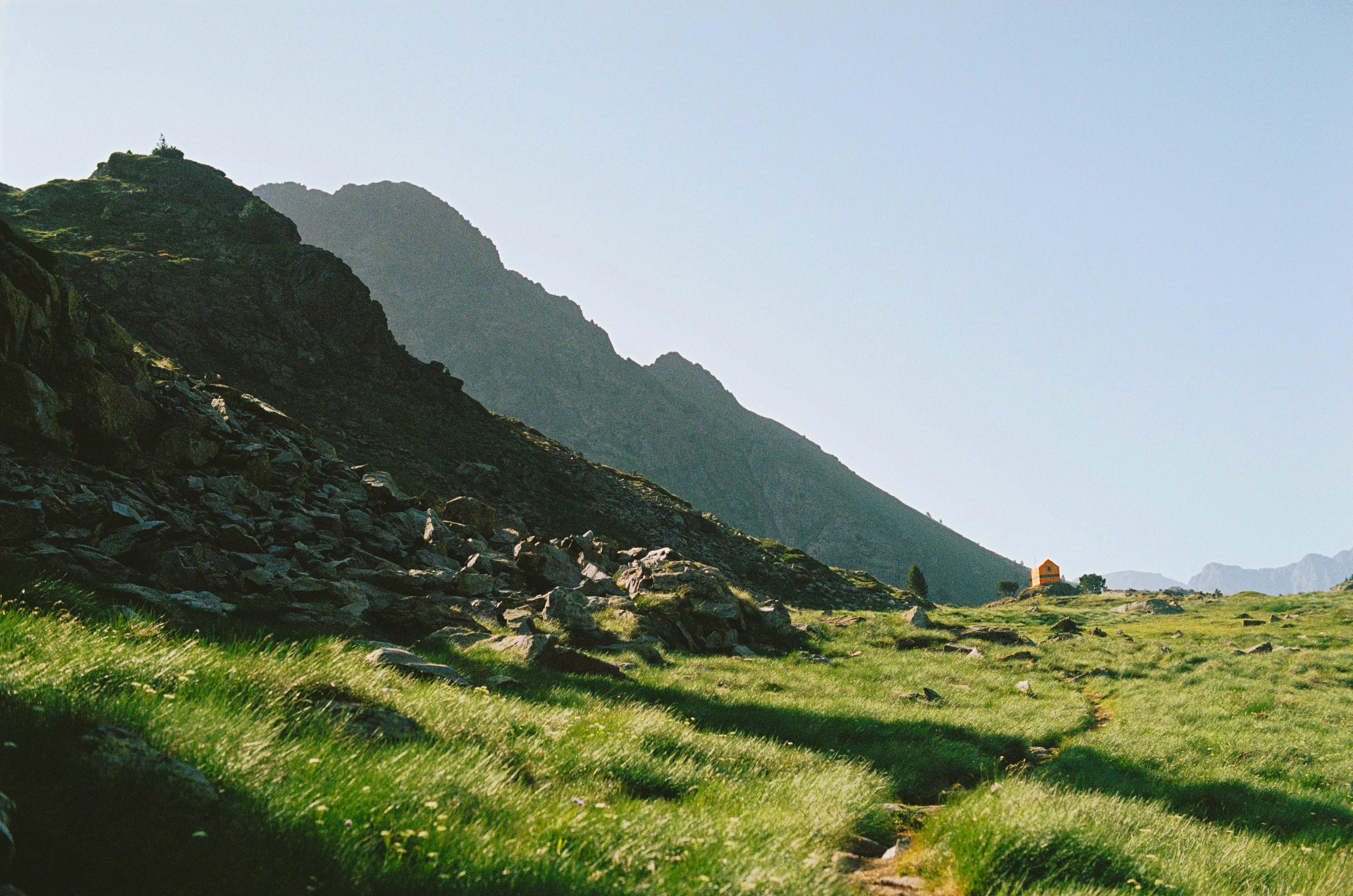 A peaceful mountain landscape in Catalonia, Spain, featuring green grass and rugged terrain under a clear sky.