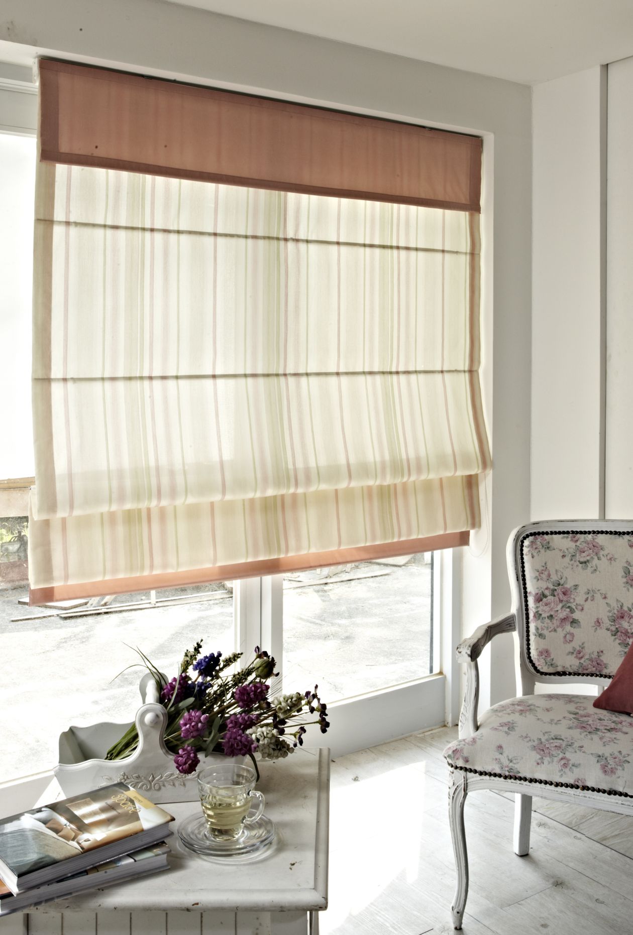 Striped roman shade beside a floral armchair in a bright classic room