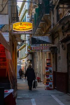 A bustling urban alley lined with Indian and Mexican restaurant signs, showcasing diverse city life.