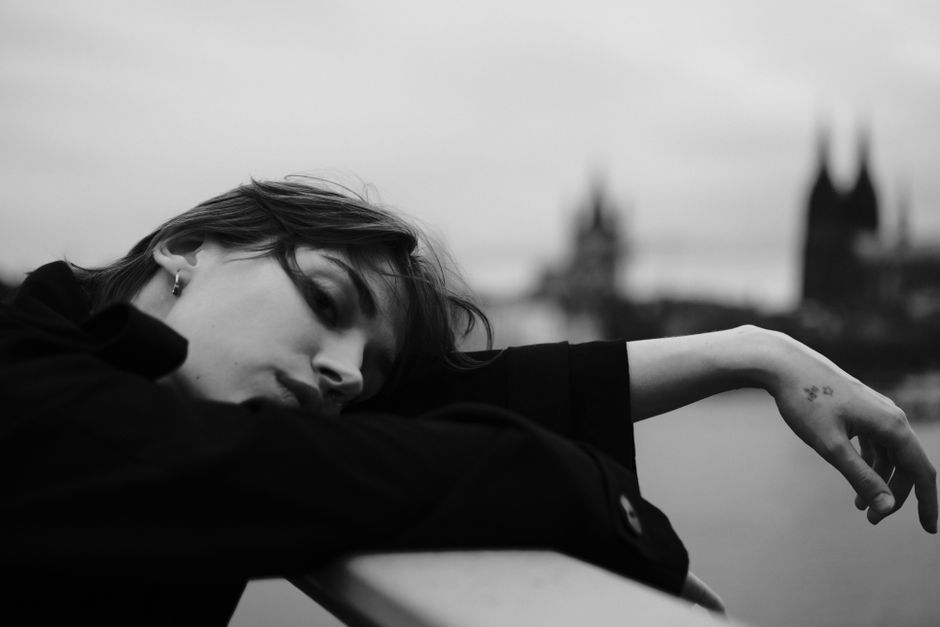 Dramatic black and white portrait of a woman on a bridge with cityscape.