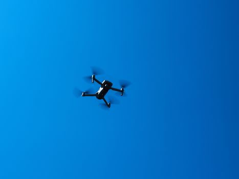 A black drone flying high in a clear blue sky, showcasing modern technology and flight capabilities.