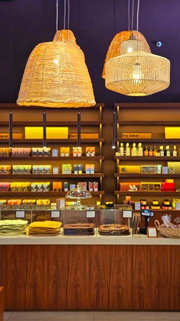 Miljöbild – A cozy gourmet shop interior with illuminated shelves and woven pendant lights.