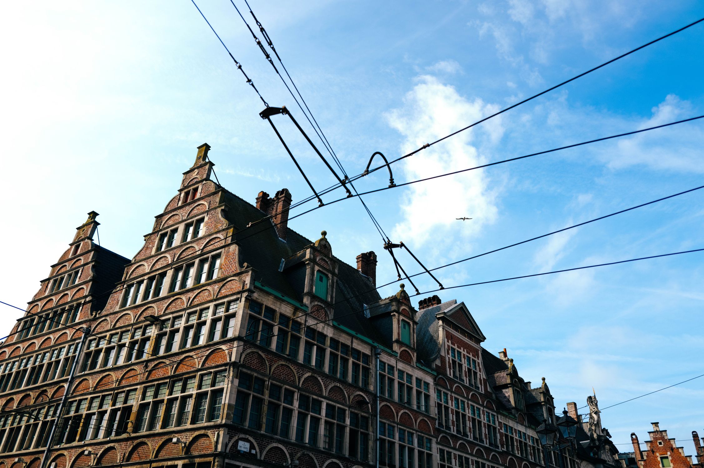 A brick gabled rooftop with overhead power lines against a sunny blue sky.