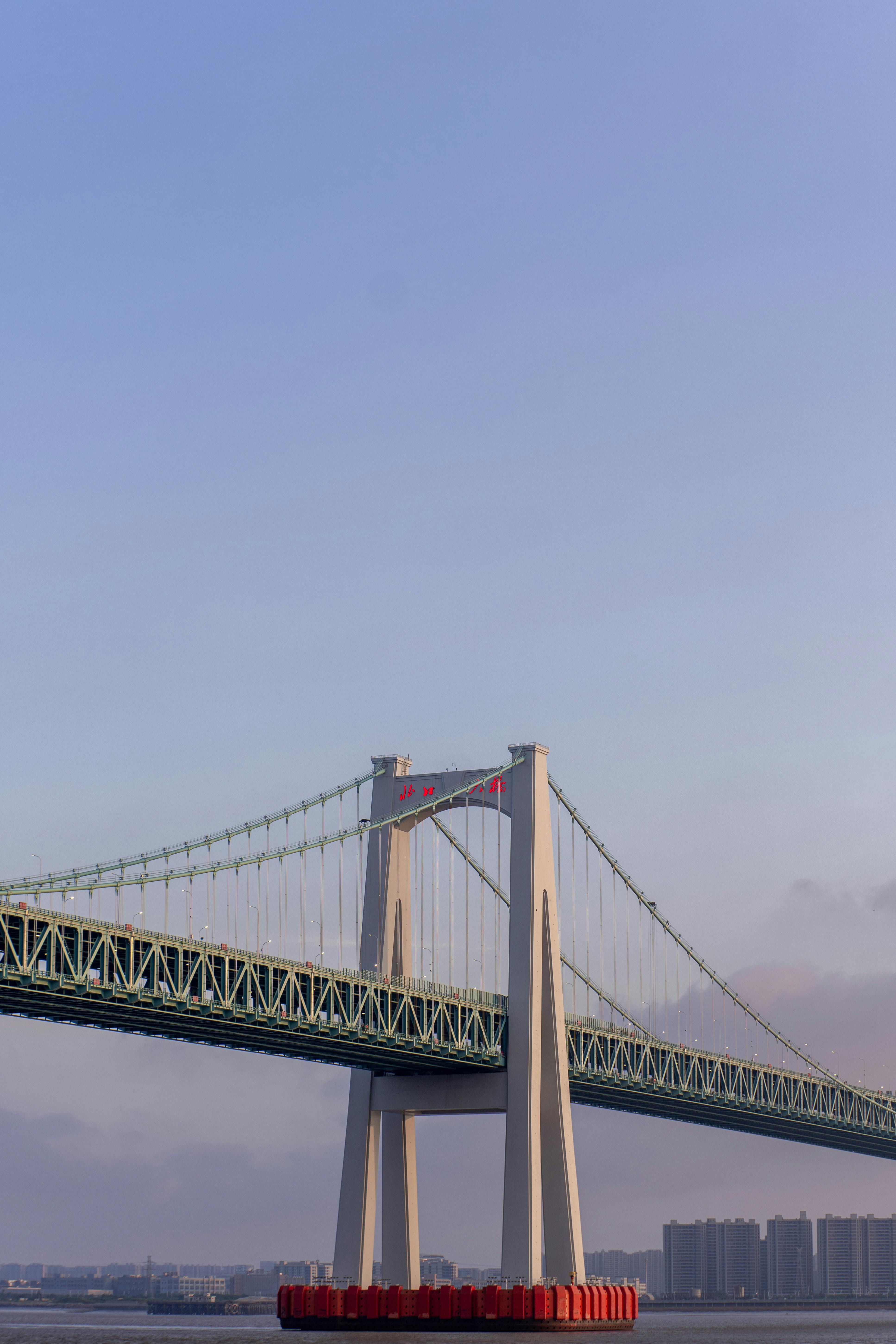 A breathtaking view of a contemporary suspension bridge silhouetted against a serene sunset sky over a tranquil river.