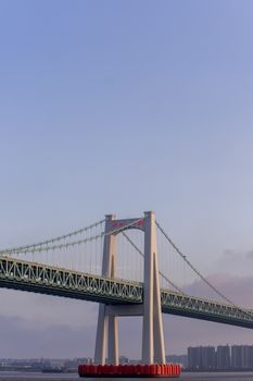 A breathtaking view of a contemporary suspension bridge silhouetted against a serene sunset sky over a tranquil river.
