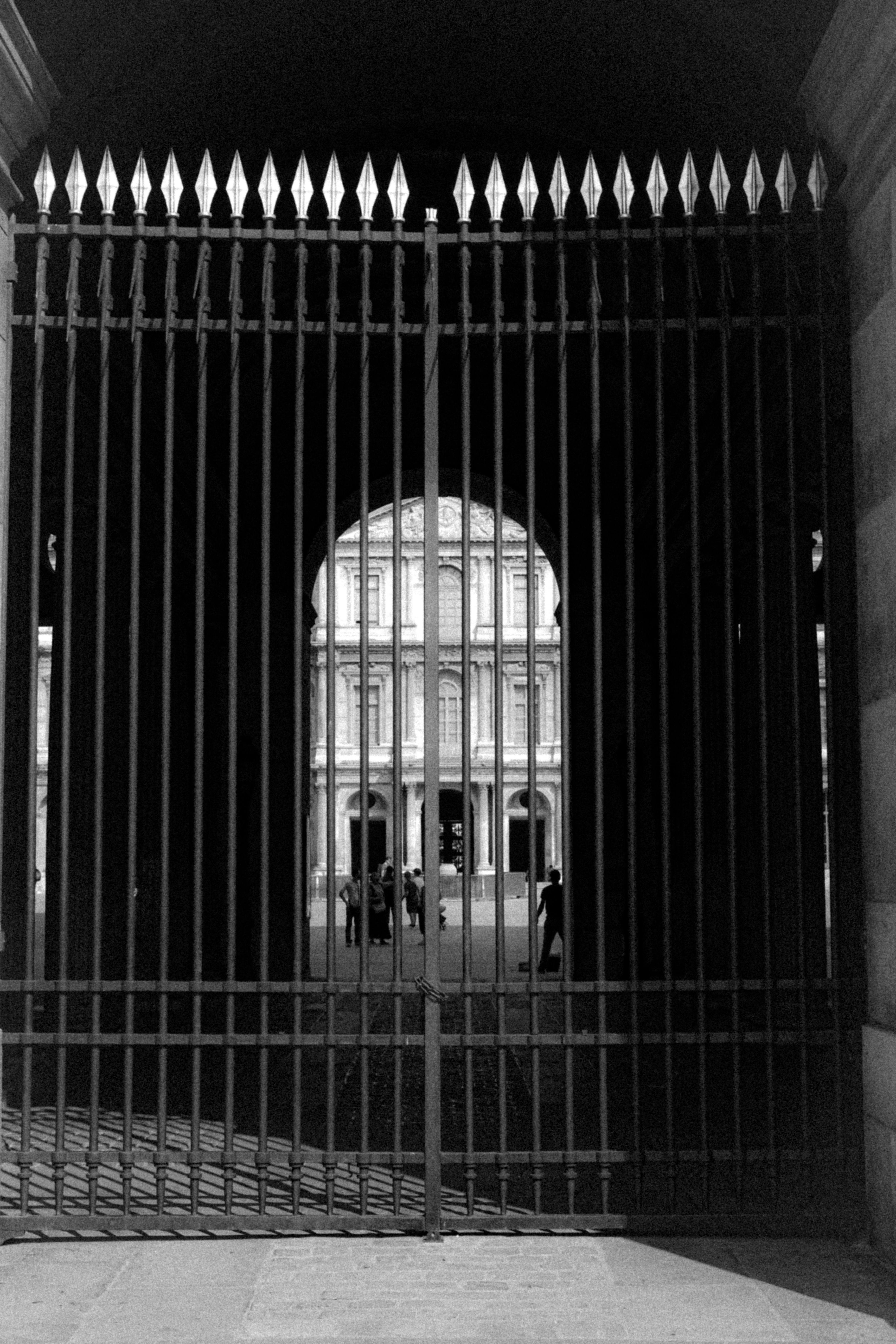 View through a large iron gate at an architectural building with people outside.