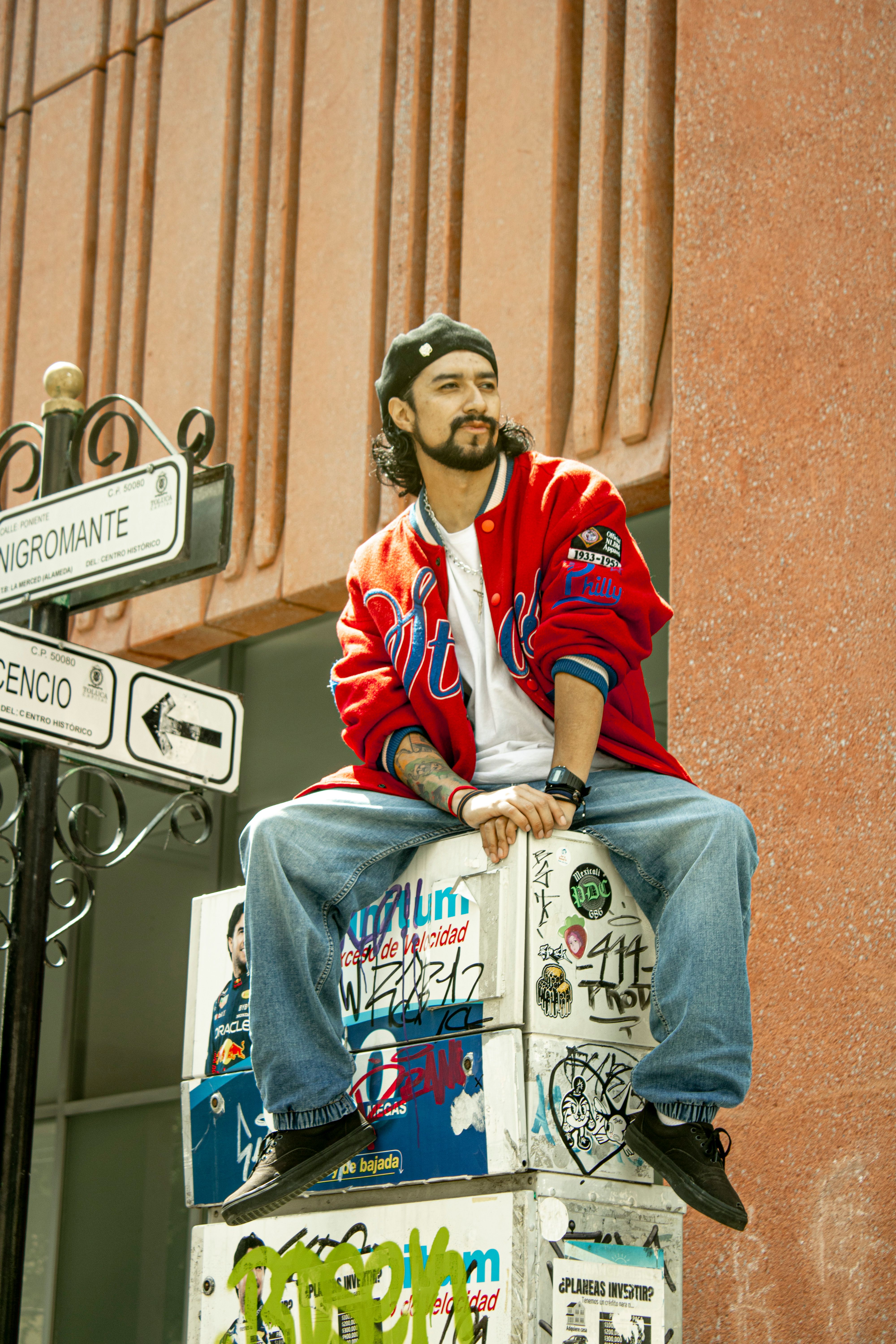 A stylish man in colorful attire sits on a graffiti-covered box in Toluca city.