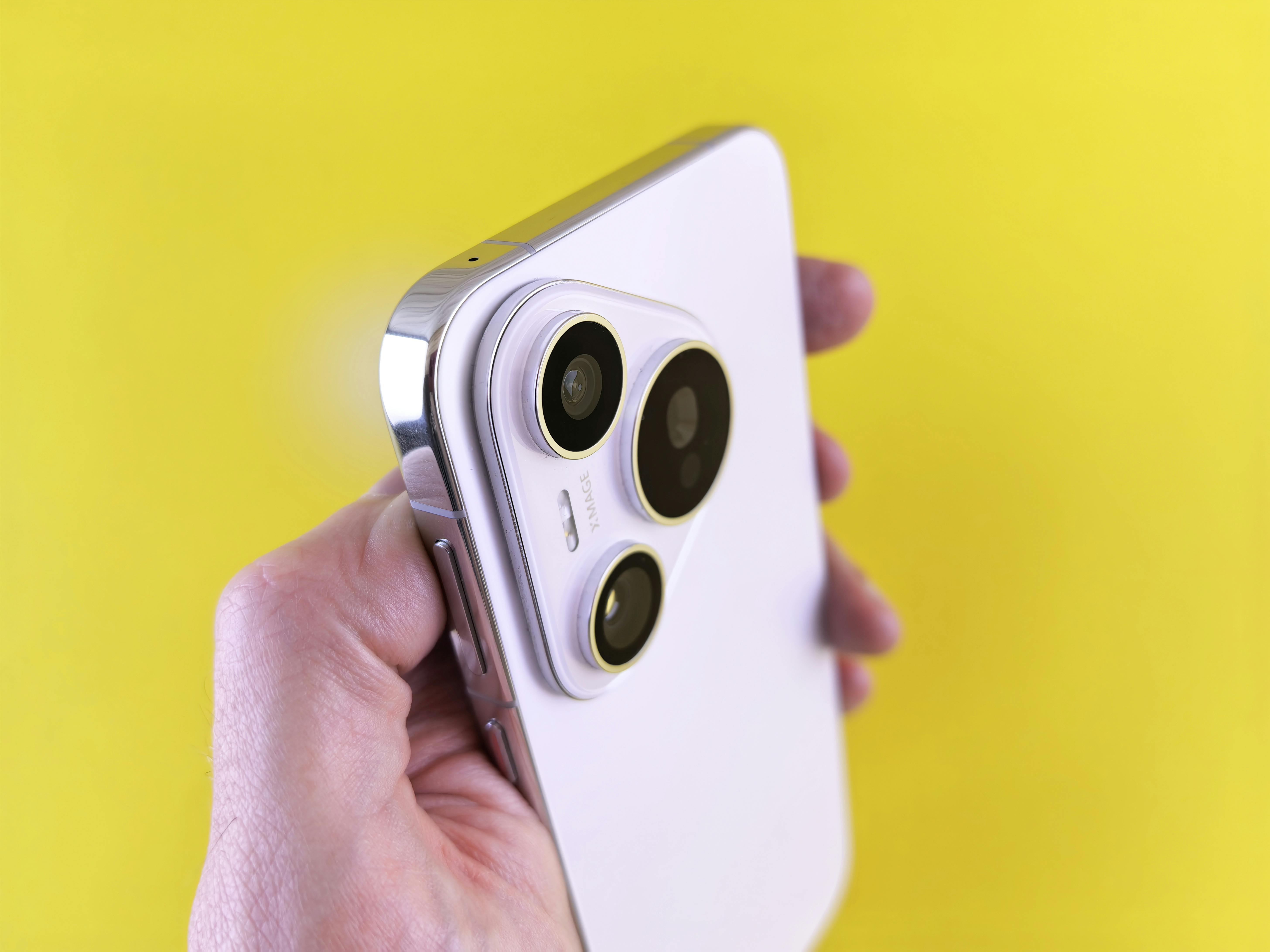 Free A close-up shot of a modern smartphone camera lens held against a bright yellow backdrop. Stock Photo