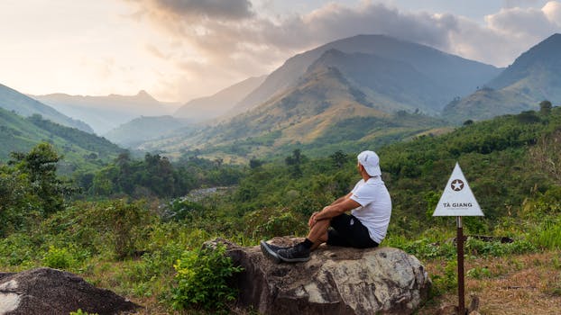 Man sitting on rock admiring scenic Tà Giang mountain view at dawn.
