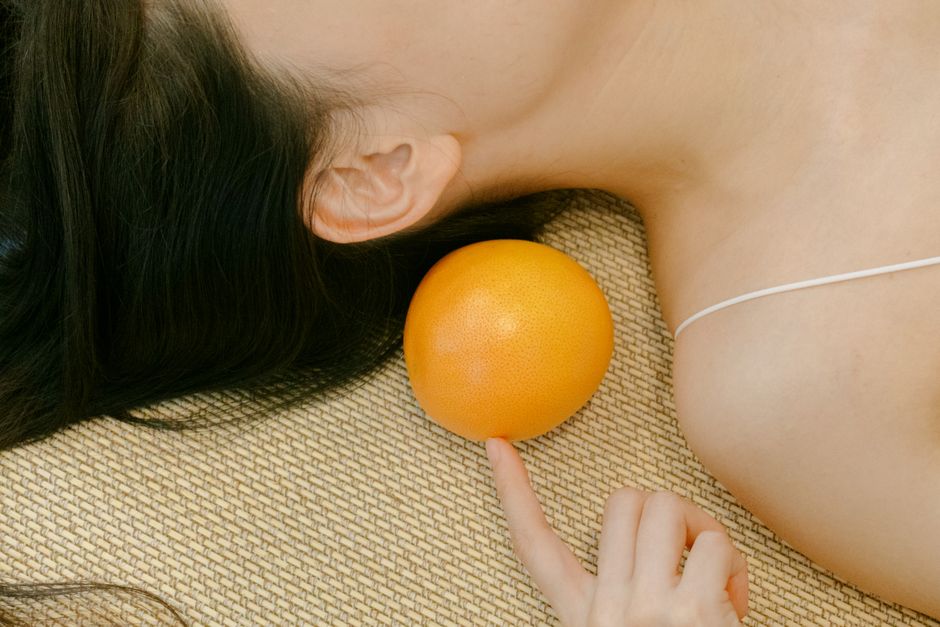 A creative composition featuring a woman lying down with a tangerine next to her. Ideal for creative concepts.