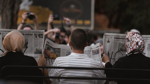 Free A candid moment of people reading newspapers on a bench in Ankara park. Stock Photo
