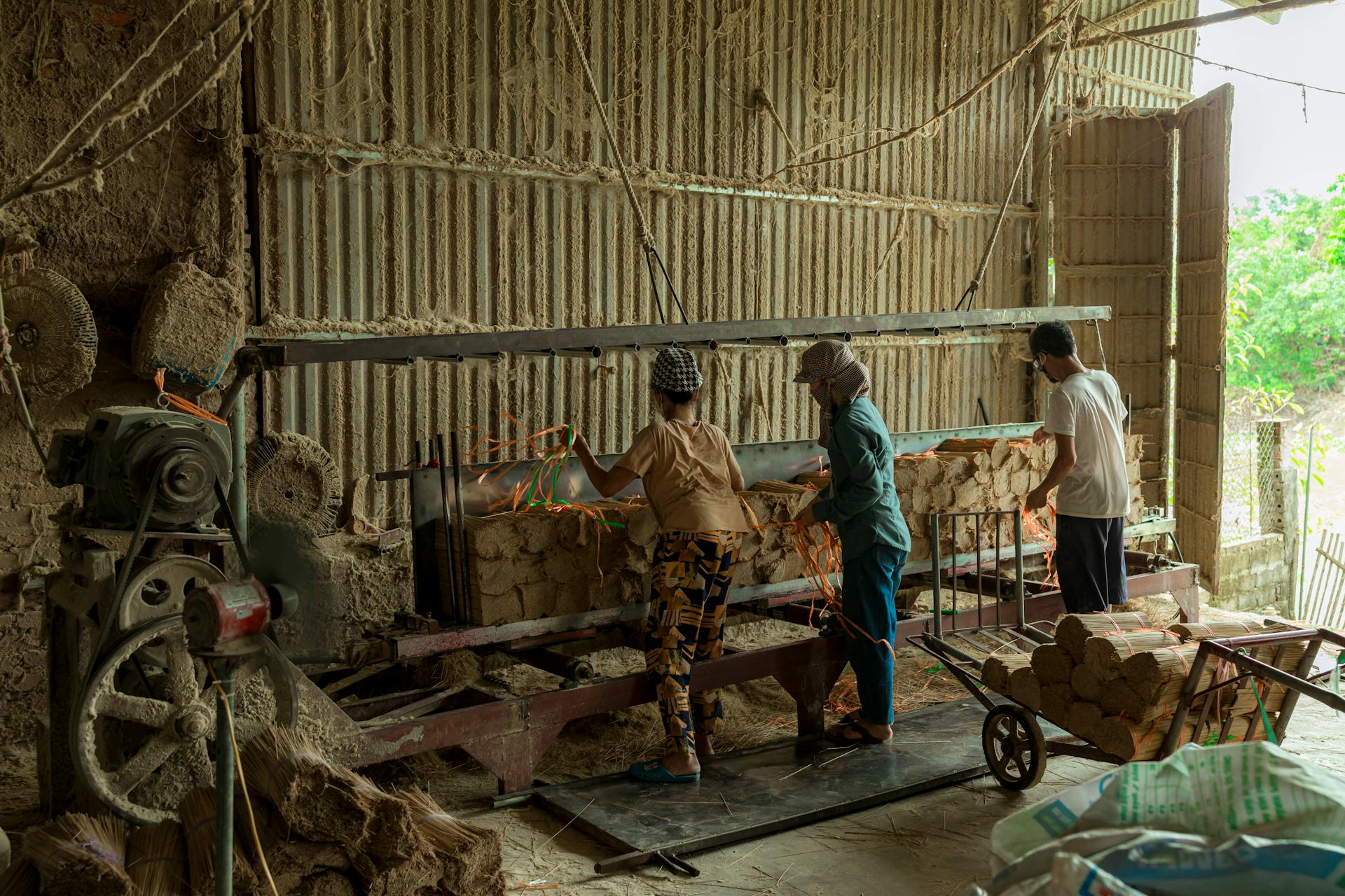 Workers in a factory managing machinery to process raw materials. Indoor industrial setting.