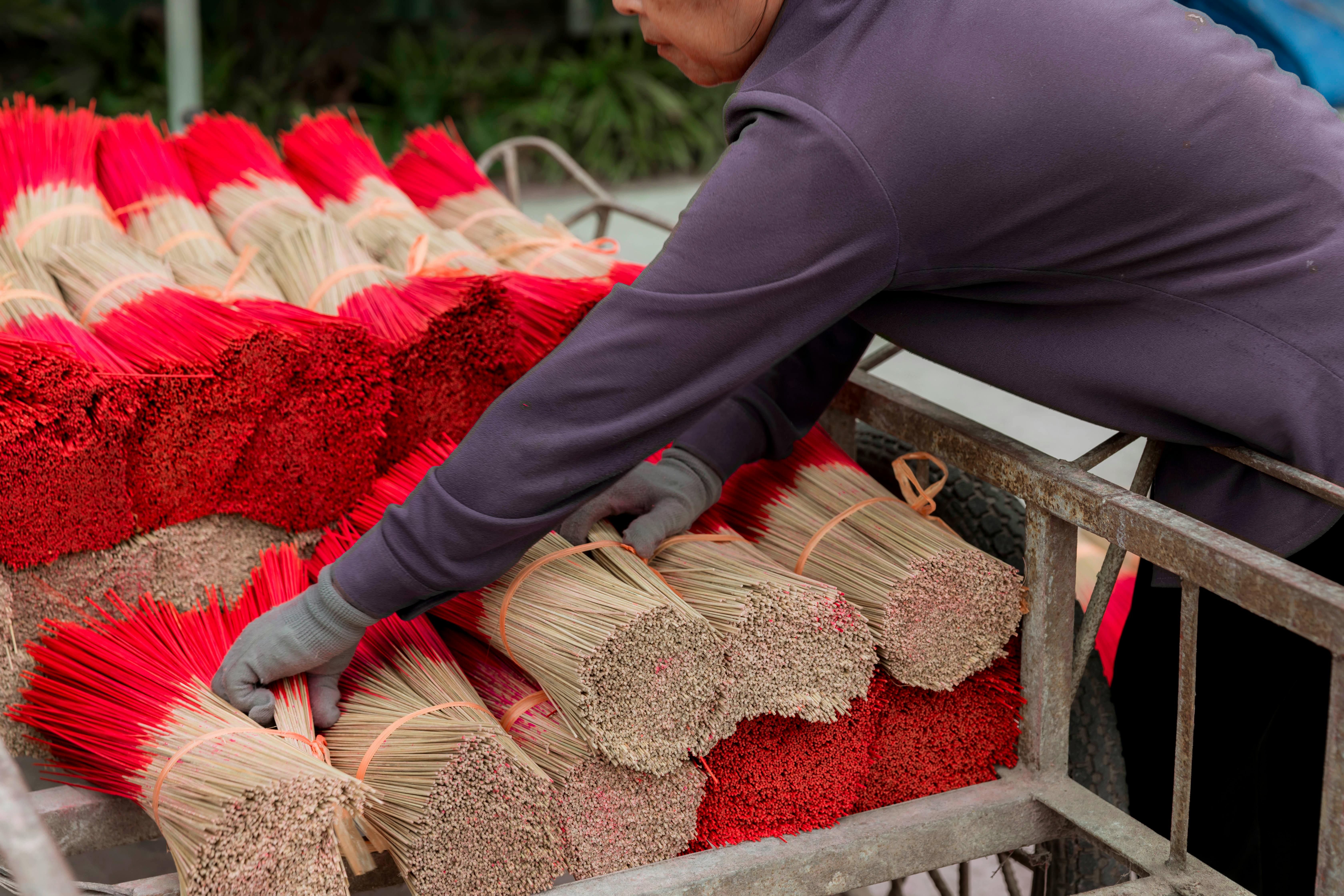A worker arranging red incense sticks in a traditional production setting.