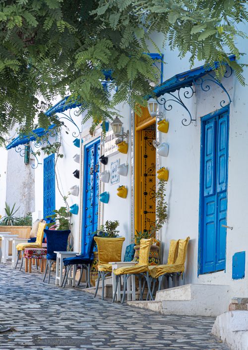 Free Inviting street view in Carthage, Tunisia, featuring vibrant blue doors and yellow chairs under lush greenery. Stock Photo