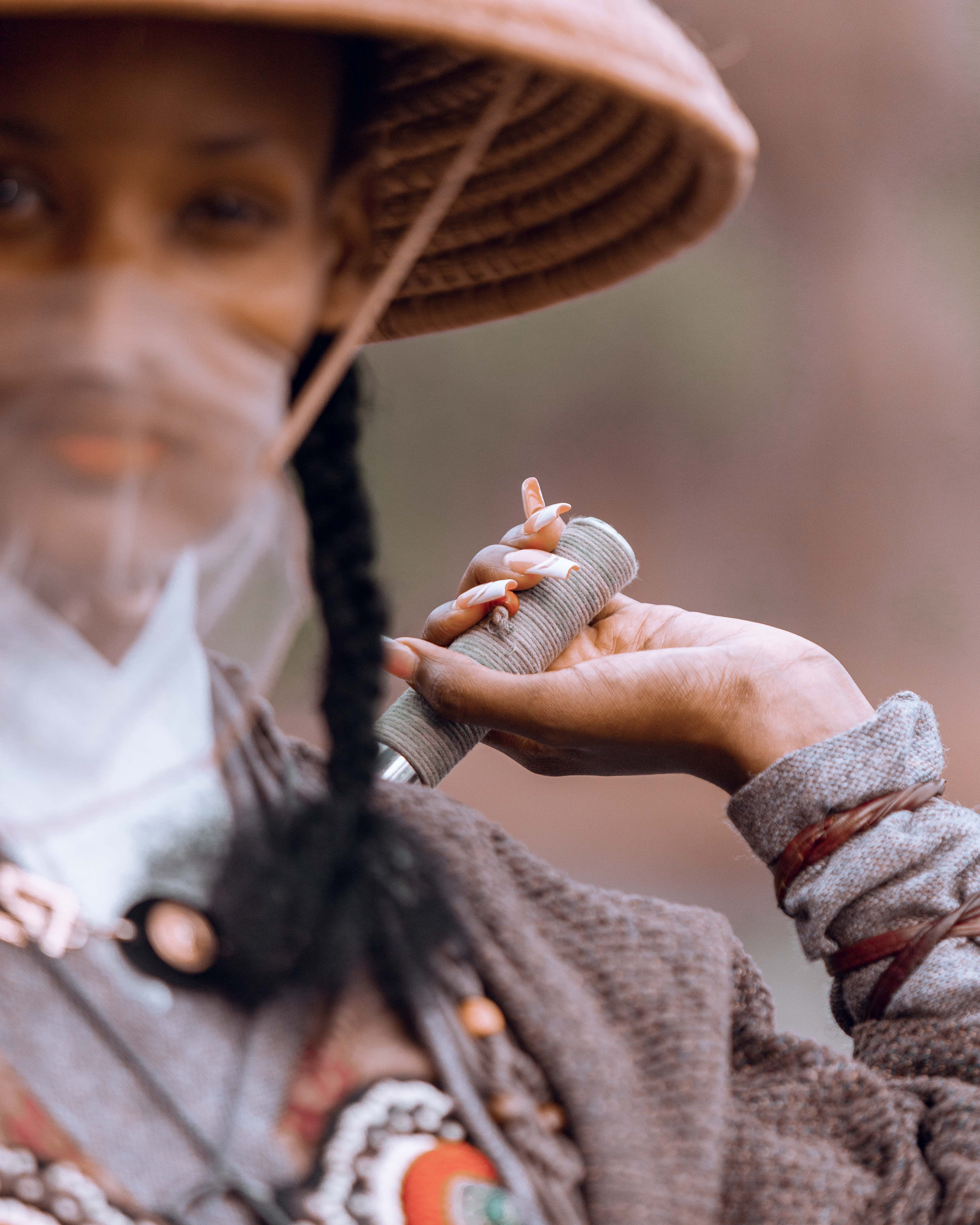 Cultural portrait of a woman wearing traditional attire and a hat, holding an object.