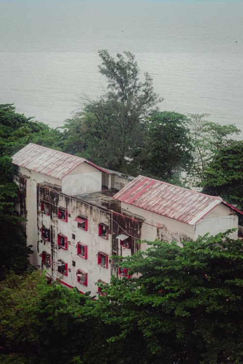 Free Old building with red windows nestled among lush trees by the coast. Stock Photo
