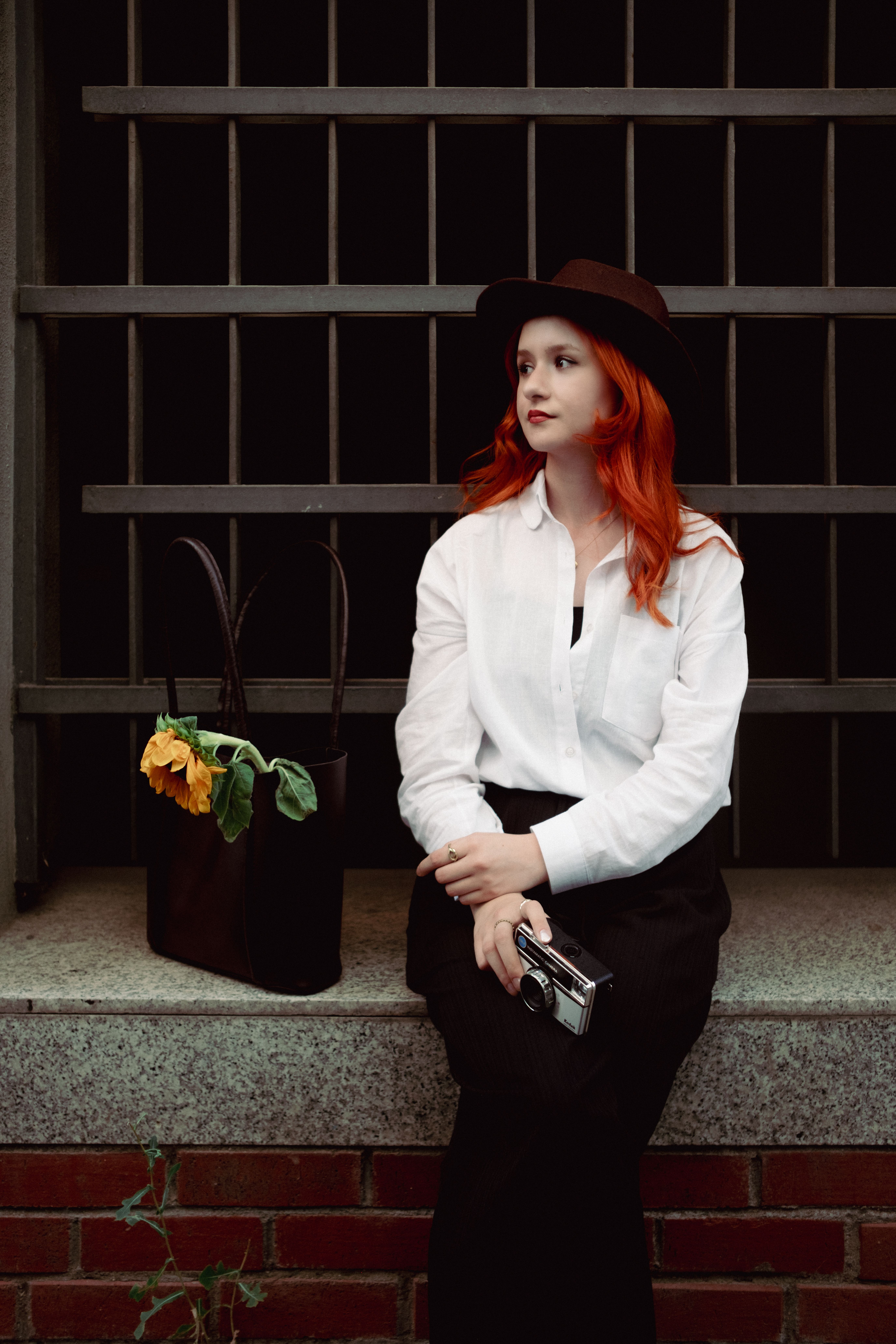 A woman with red hair sitting on a ledge with a bag · Free Stock Photo