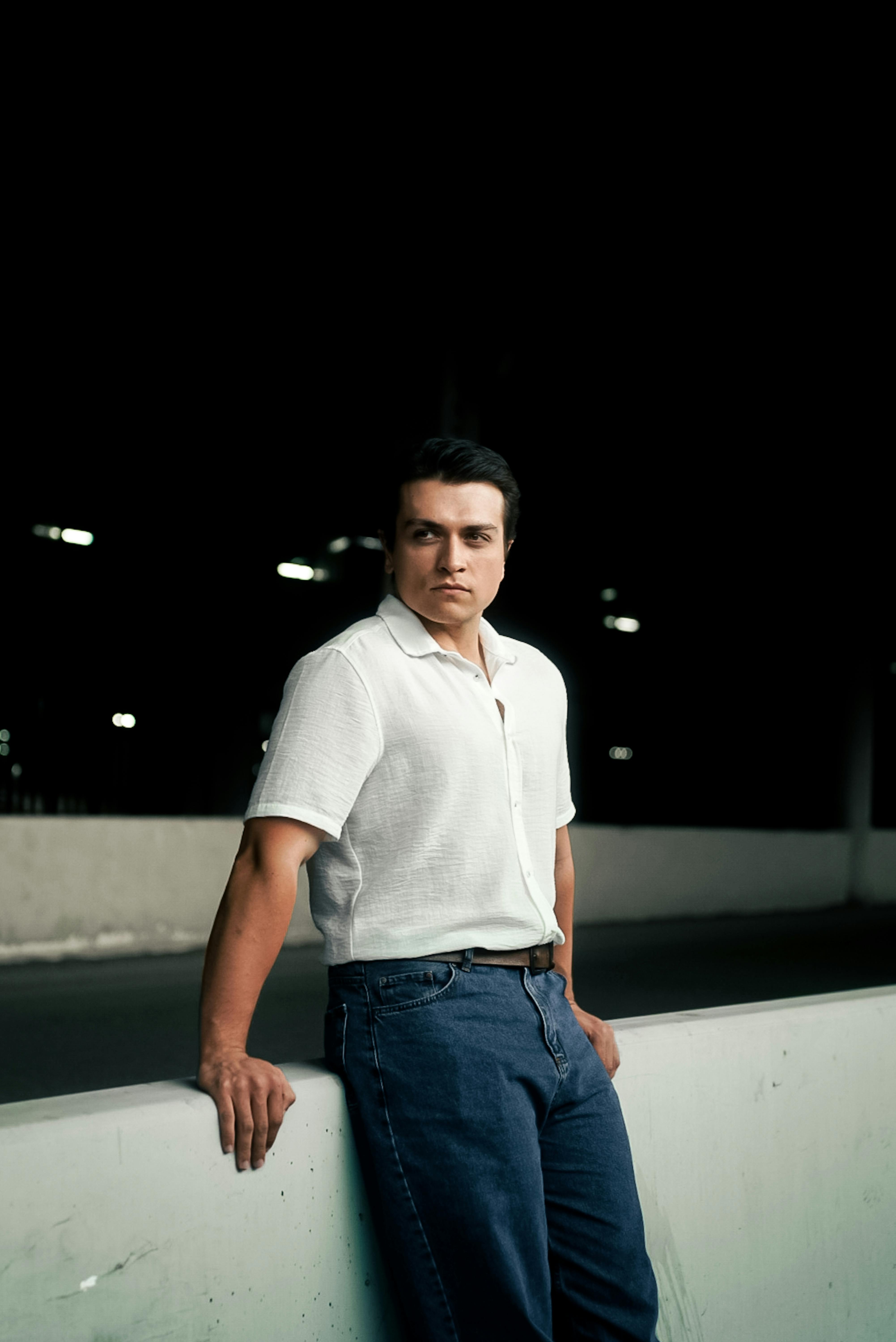 a man in jeans leaning against a wall