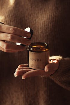 Warm candlelight captured as a wooden cap reveals 'Hygge' candle, perfect for fall coziness.