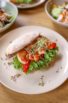 Close-up of a delicious sandwich with salmon, lettuce, and sprouts on a plate.