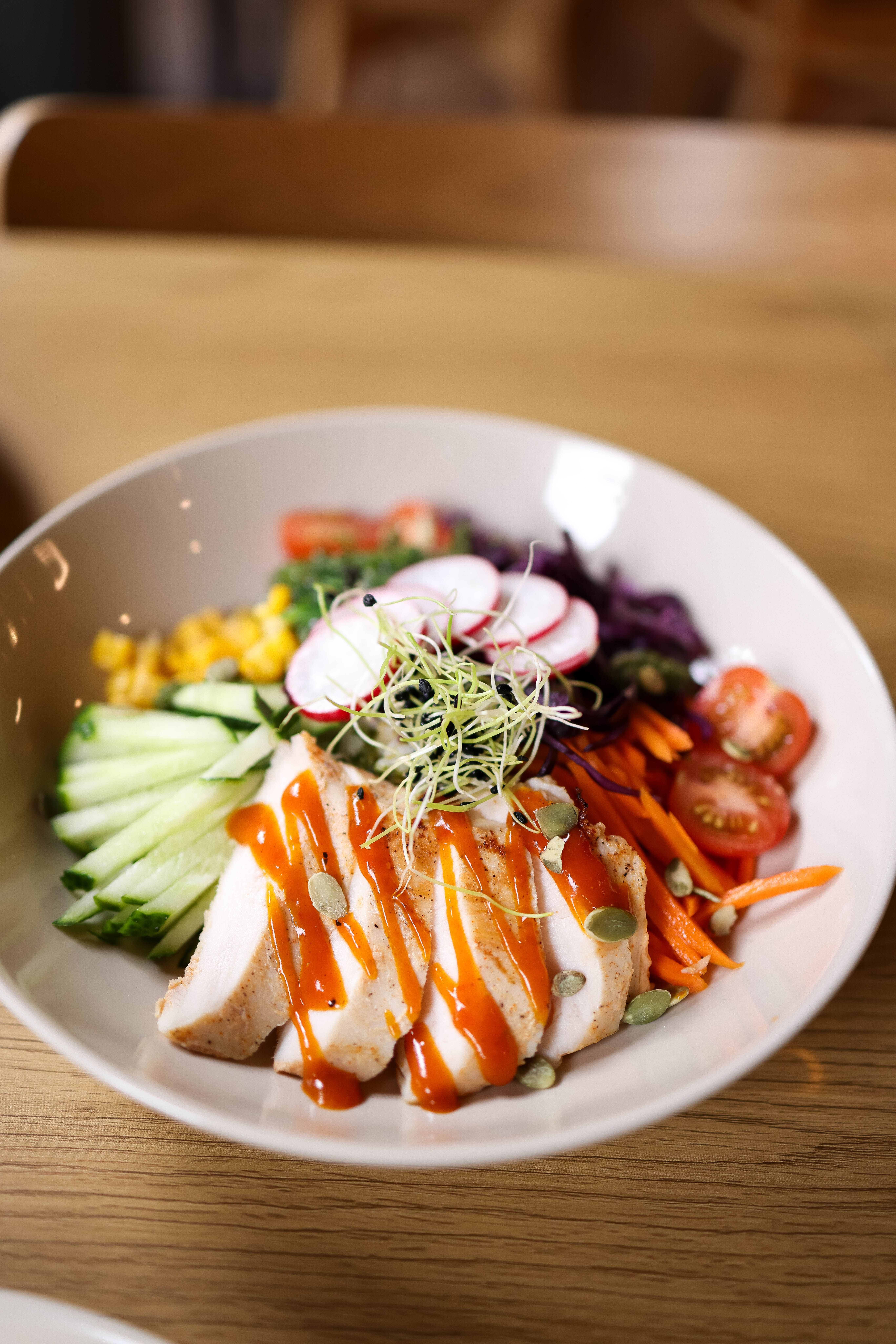 A rice bowl with cilantro-lime rice, sliced grilled chicken breast, charred corn kernels, black beans, and a drizzle of orange-red habanero crema, topped with fresh cilantro and thinly sliced radishes.