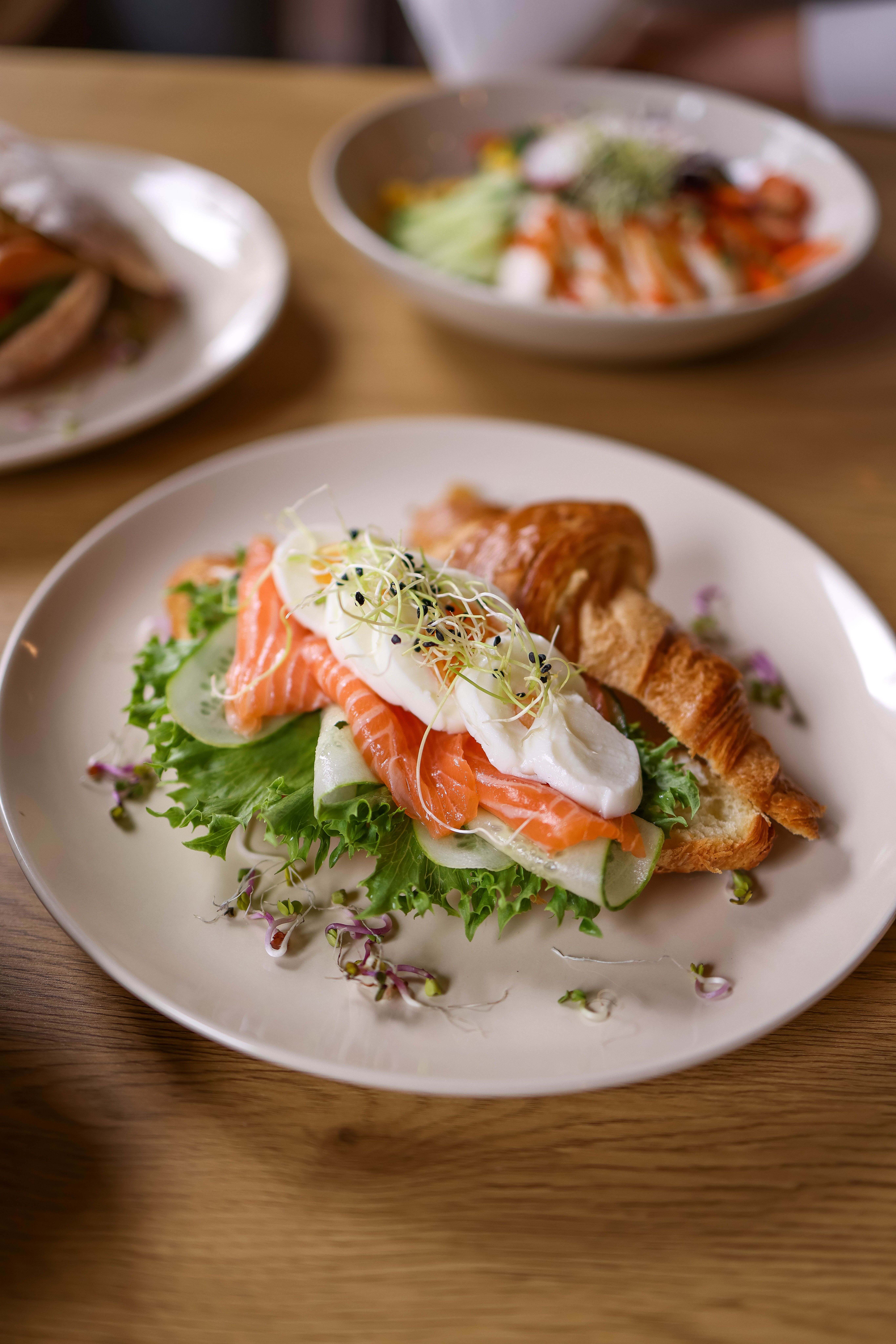 A delectable croissant topped with salmon, lettuce, cucumber, and sprouts on a plate.