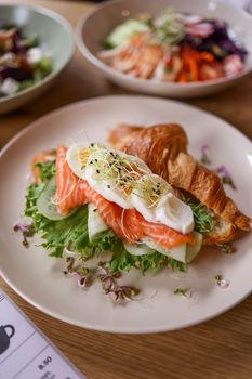 A gourmet croissant sandwich with fresh salmon, cream cheese, and sprouts served on a plate.