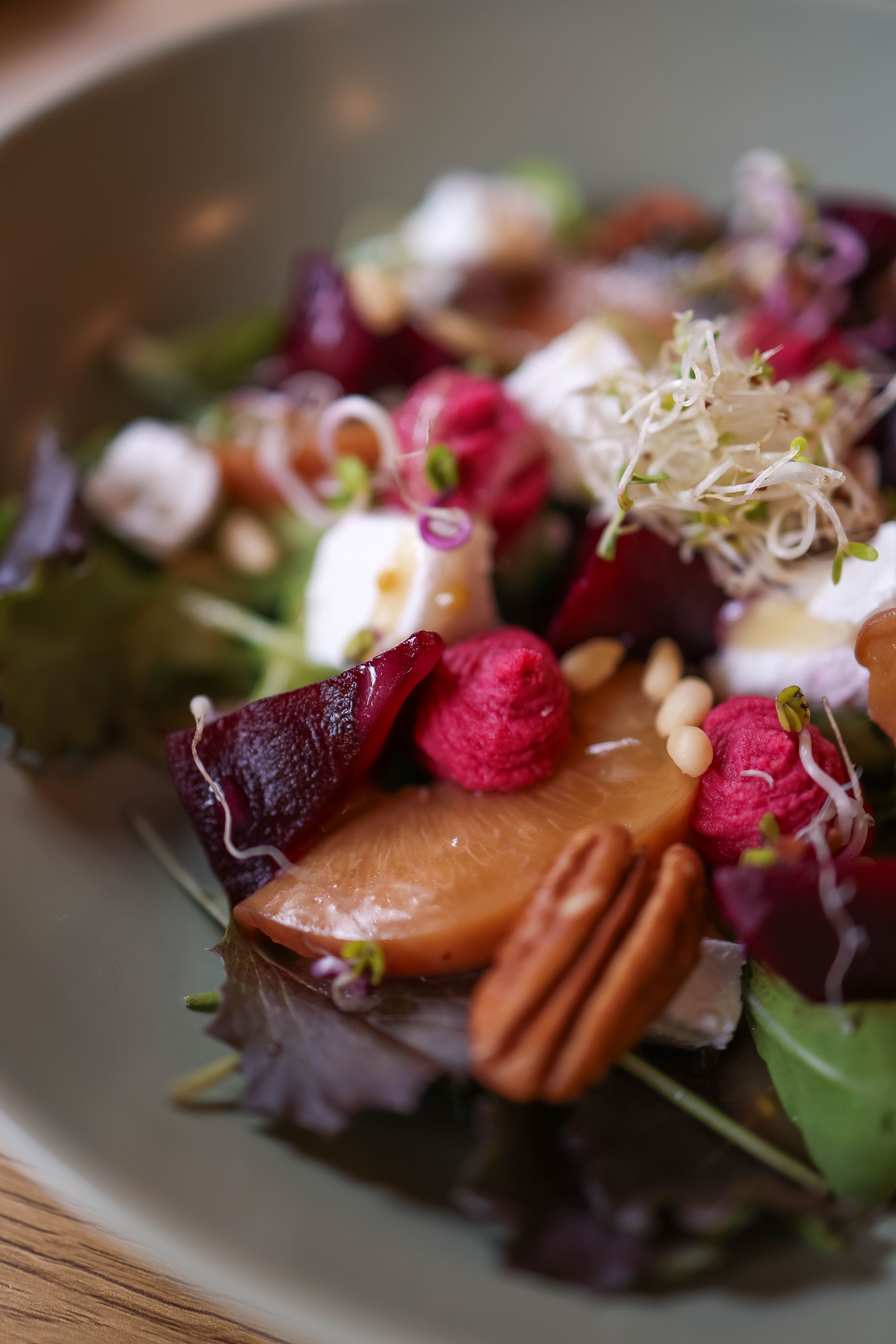 A vibrant autumn salad with fresh beets, nuts, and sprouts on a green plate.