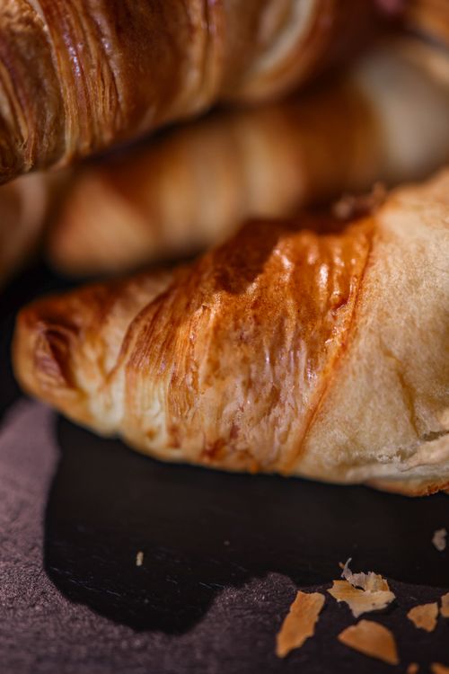 Free A close-up image of golden, flaky croissants on a dark surface, capturing their buttery layers. Stock Photo