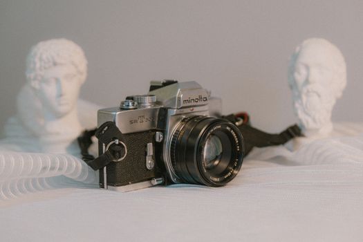 A vintage Minolta camera next to classical sculptures, capturing a nostalgic and artistic atmosphere.