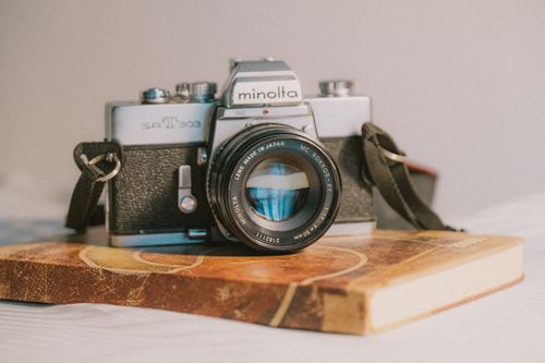Free A vintage Minolta camera rests on a vintage book, showcasing timeless analog photography style. Stock Photo