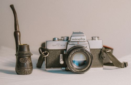 Free A classic Minolta SLR camera paired with a carved wooden pipe, embodying retro nostalgia. Stock Photo