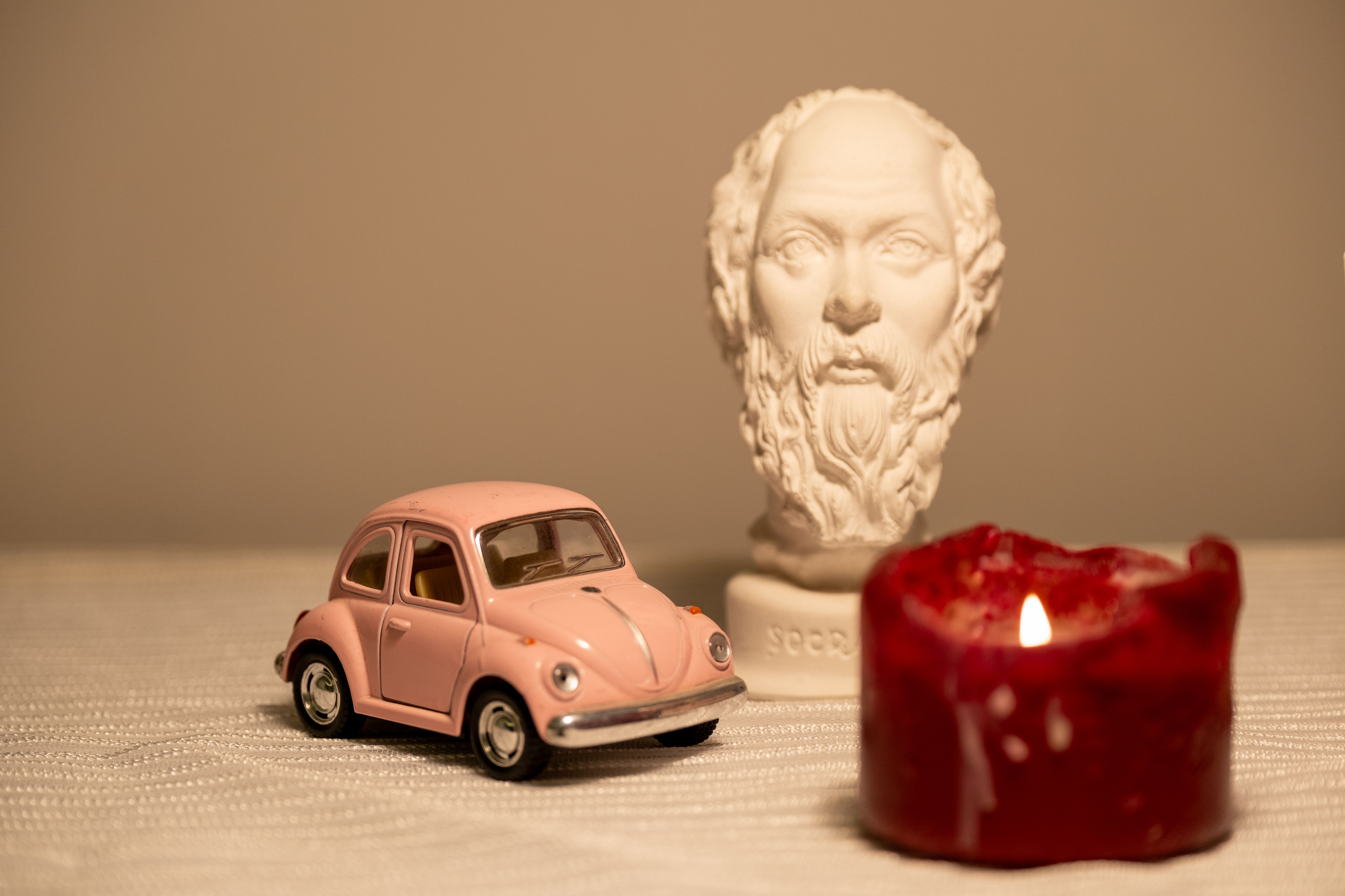 Artistic setup of a pink toy car, bust statue, and candlelight creating a nostalgic vintage ambiance.